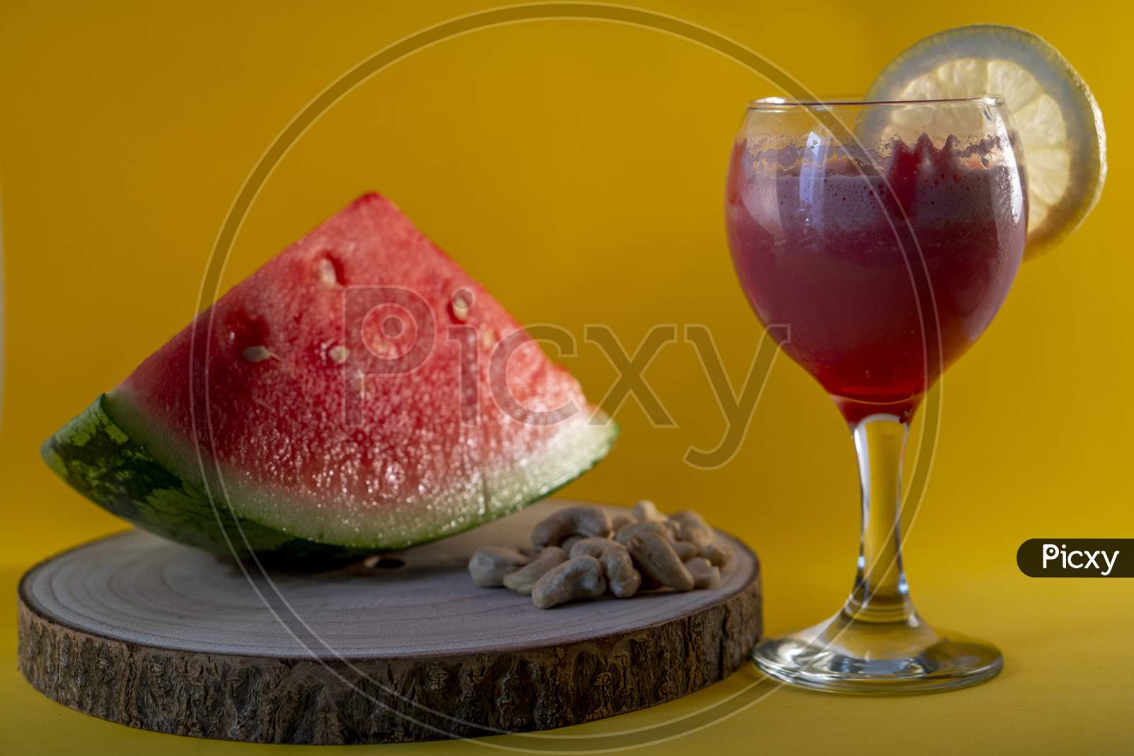 Fresh watermelon juice with a lemon slice, a watermelon piece and Cashew nuts on a yellow background.