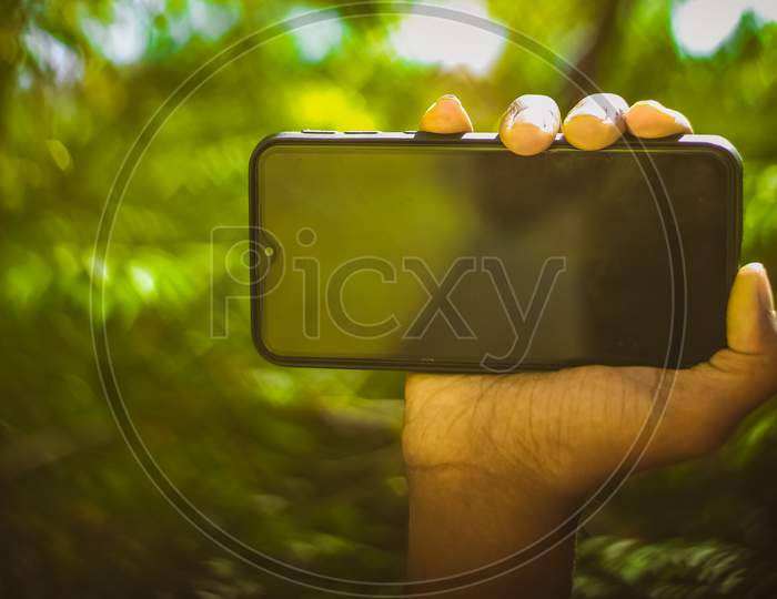 Boy Hand Showing Mobile Smart Phone Screen Isolated On Blur Green Nature Background.