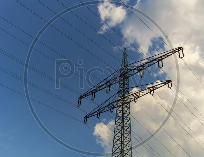 A Power Mast Below A Blue,Cloudy Sky