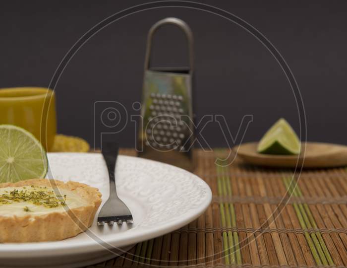 Side View Of Lemon Tart On Dish Plate With Lemon Slices On Table.