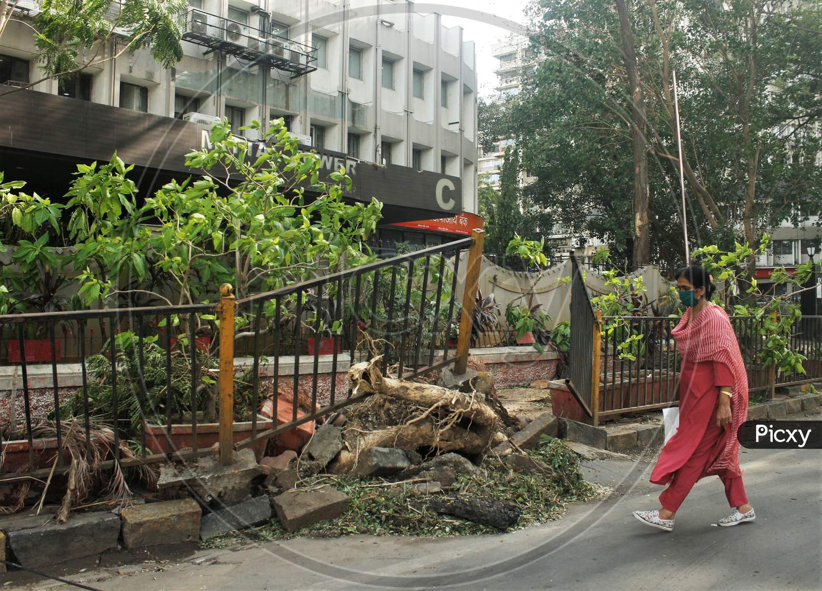 A woman walks past an uprooted pavement railing, after cyclone Nisarga made its landfall on June 3, on the outskirts of the city, in Mumbai, India, June 5, 2020.
