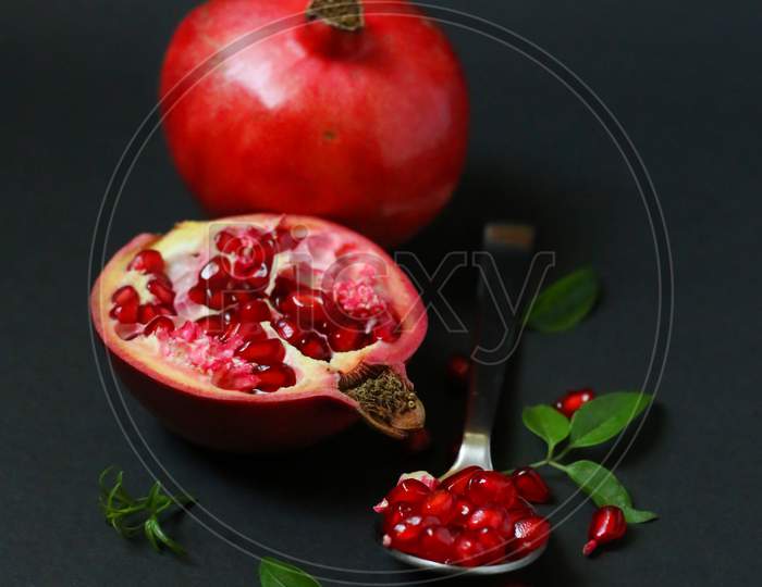 Ripe pomegranate fruit with seeds and leaves on dark background