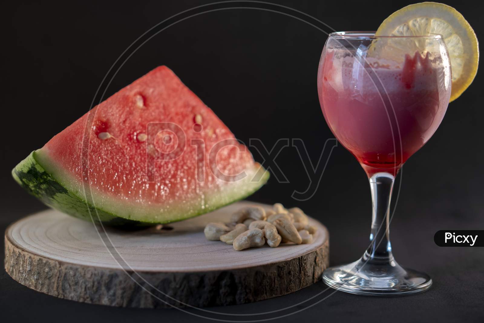 Fresh watermelon juice with a lemon slice, a watermelon piece and Cashew nuts on a black background.