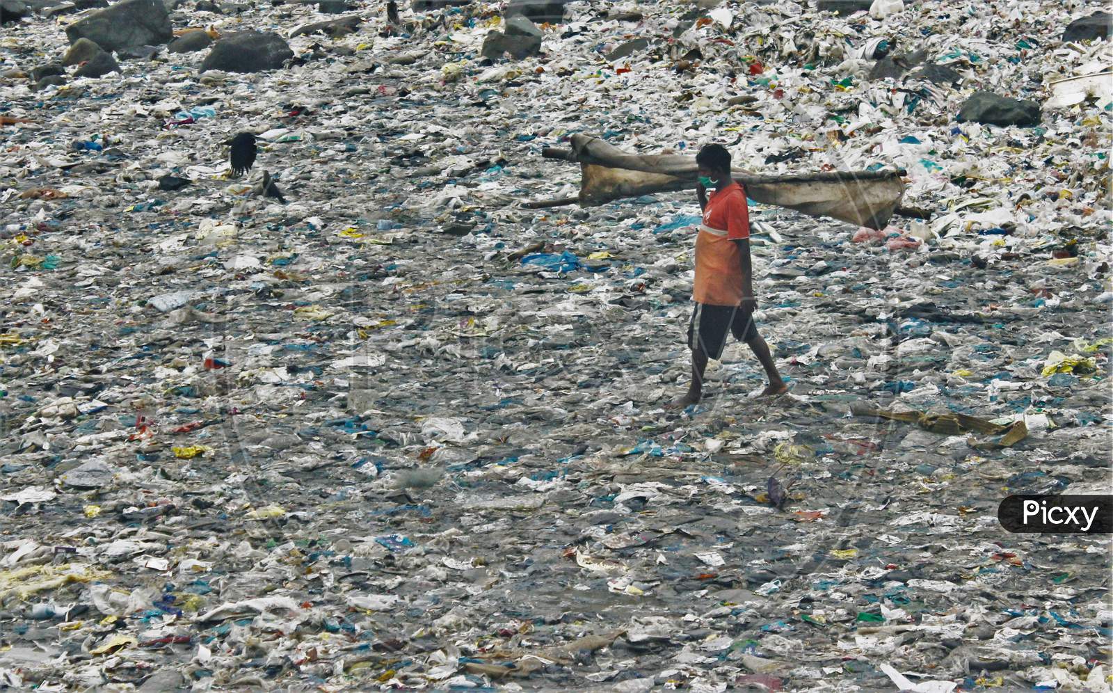 A fisherman walks on a beach covered with plastic waste to go to the sea to wash a cloth used to cover boats on the occasion of World Environment Day, in Mumbai, India on June 5, 2020.