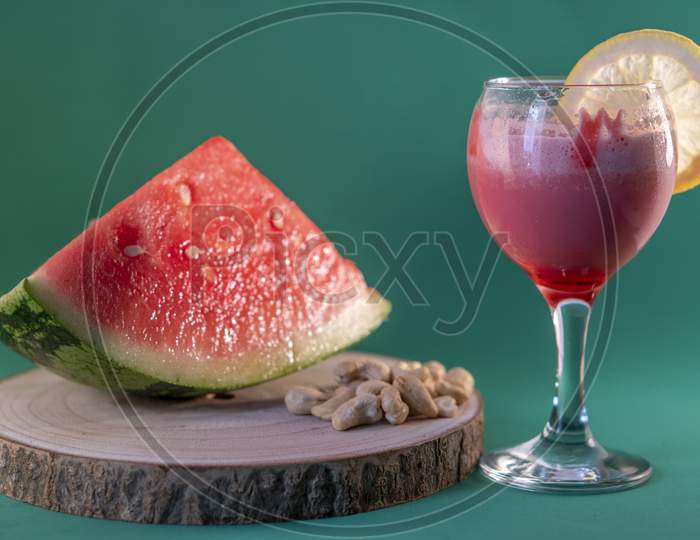 Fresh watermelon juice with a lemon slice, a watermelon piece and Cashew nuts on a green background.