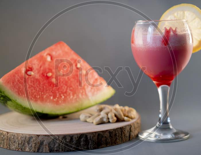 Fresh watermelon juice with a lemon slice, a watermelon piece and Cashew nuts on a grey background.