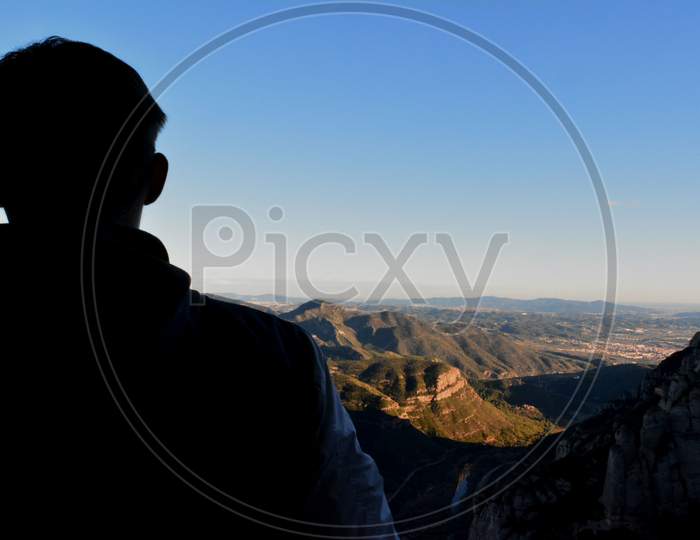 Back view of a man sightseeing hills from a mountain top shown in a blur background.