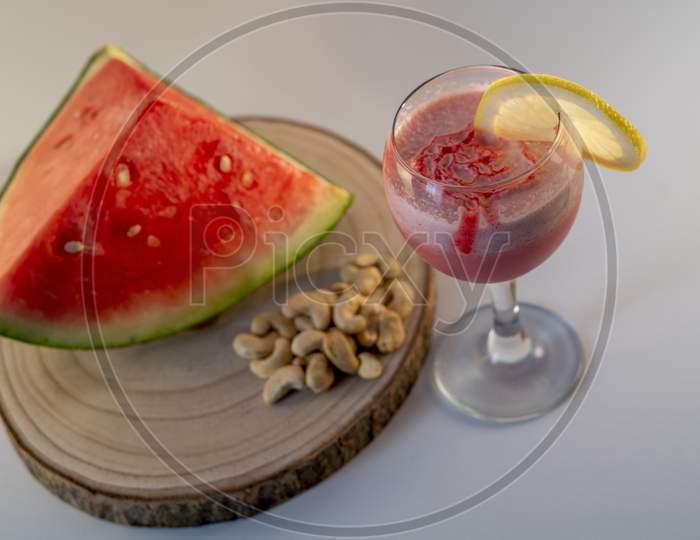 Fresh watermelon juice with a lemon slice, a watermelon piece and Cashew nuts on a white background.