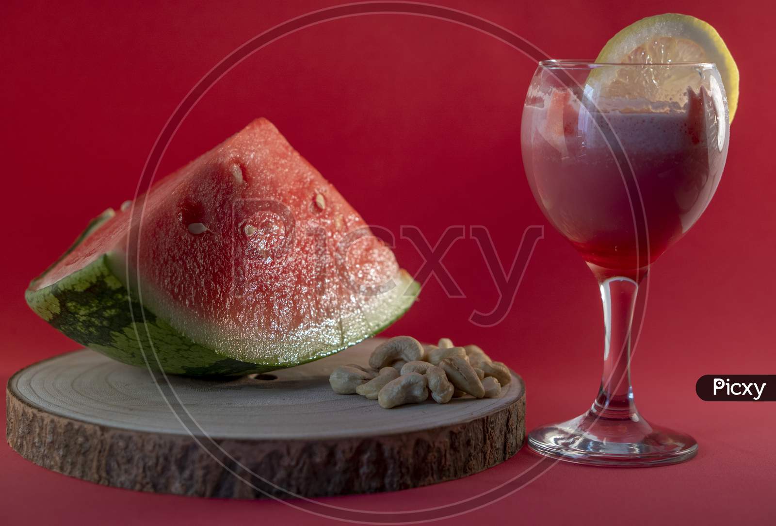 Fresh watermelon juice with a lemon slice, a watermelon piece and Cashew nuts on a red background.