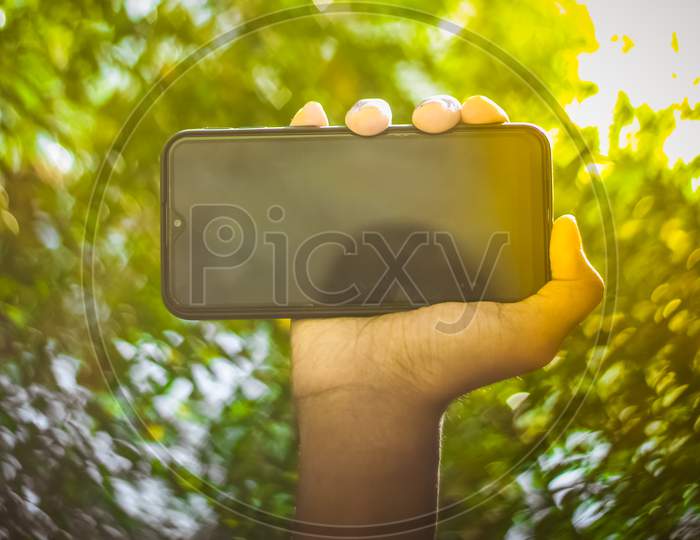 Boy Hand Showing Mobile Smart Phone Screen Isolated On Blur Green Nature Background.