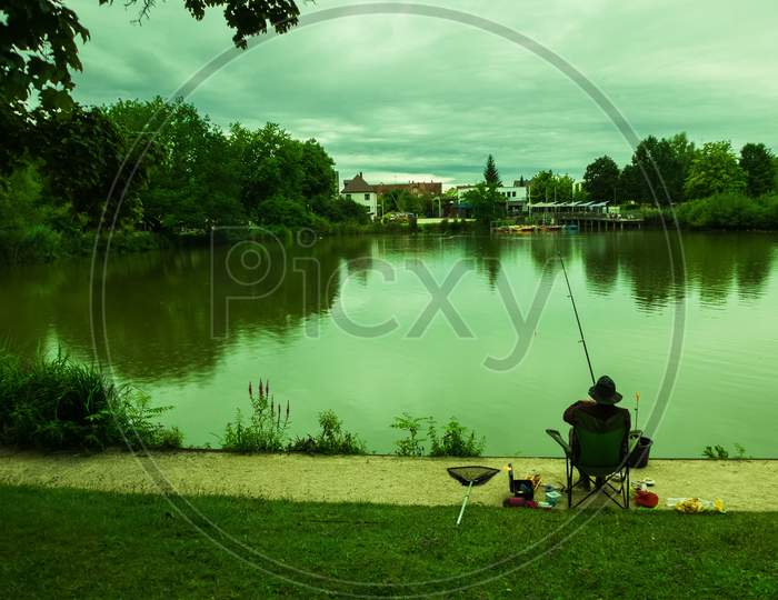 An Angler Was Fishing On A Small Lake On A Cloudy Afternoon