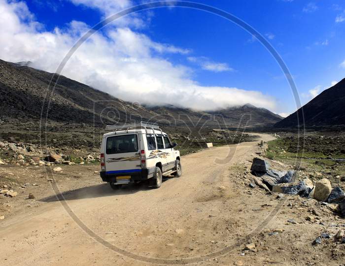 A Vehicle moving on a Path with mountains of Sikkim in the Background