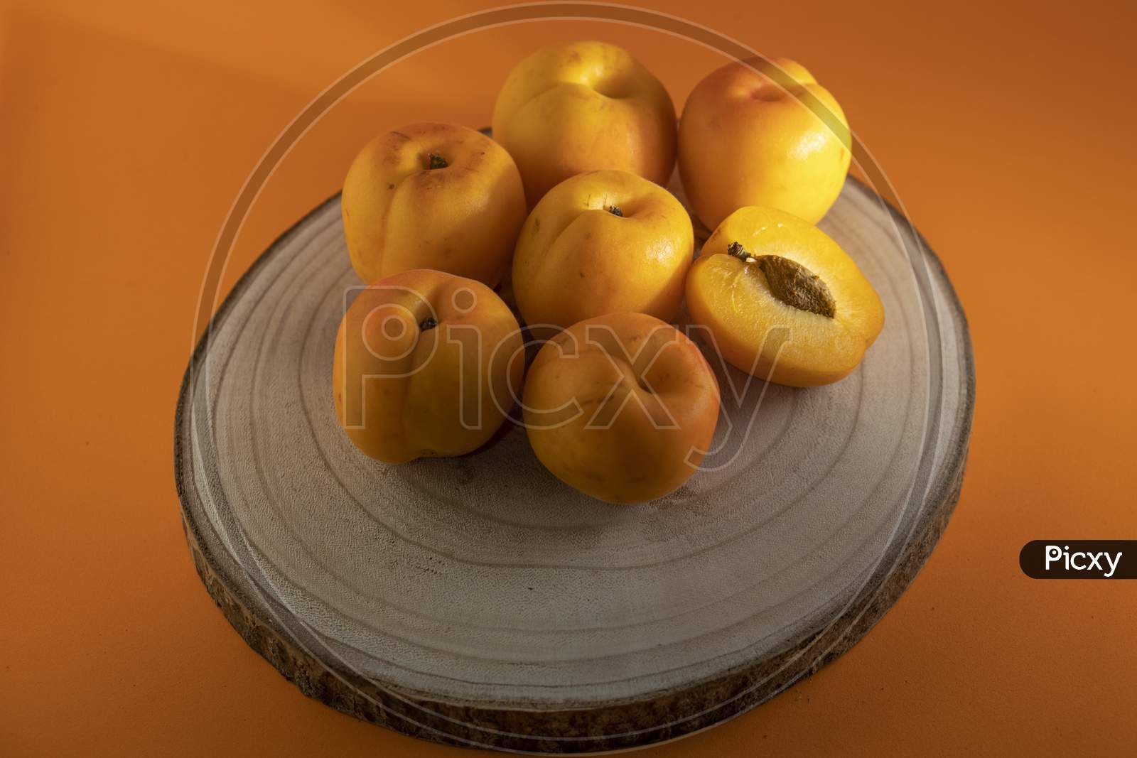Peach on a wooden dish and an orange background.