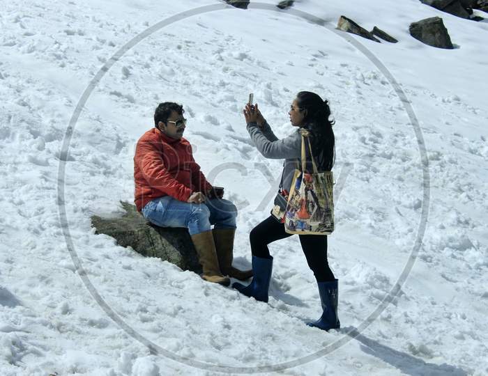 Tourists clicking photos by sitting on a Snow Capped Mountain