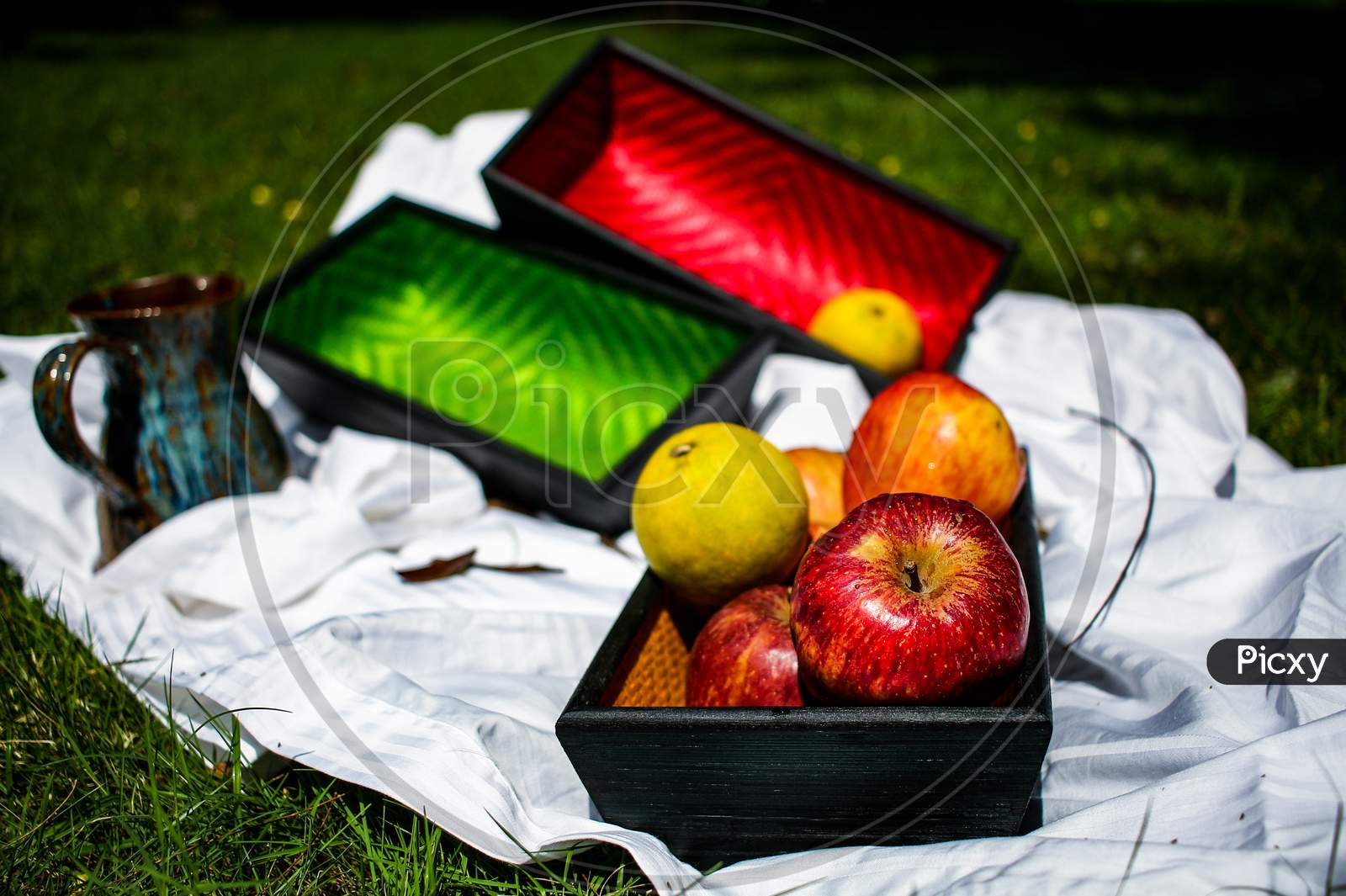 Still Life Of Apples On A Wooden Tray With Two More Colorful Trays In The Background.