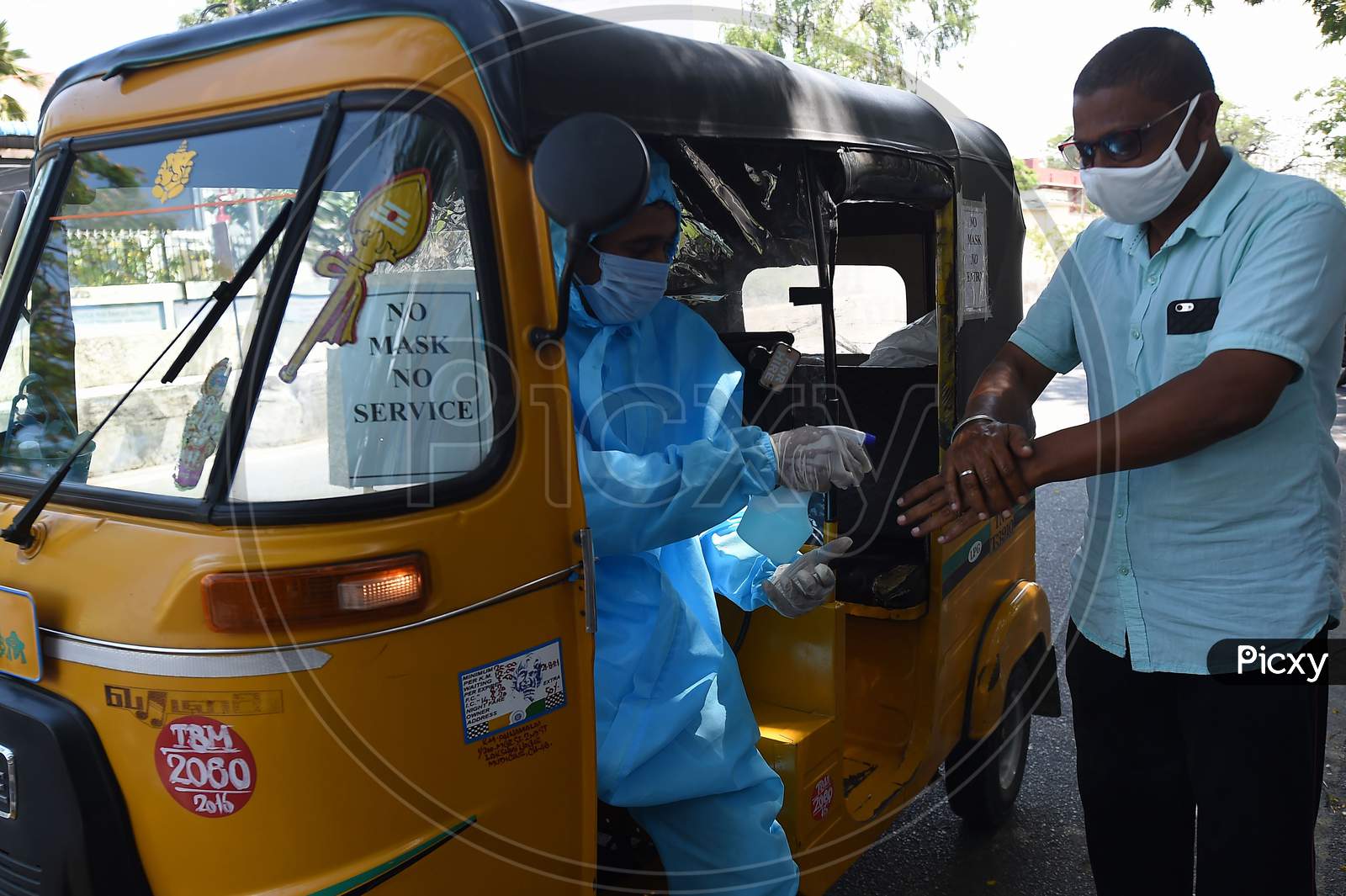 An Auto Rickshaw Driver Wearing Personal Protective Equipment  (Ppe) Sprays Sanitiser On The Hands Of A Customer in Chennai, Tamil Nadu