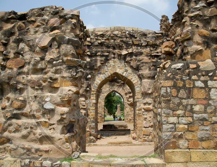 Remains Of Walls And Arches At The Qutub Complex In India. Looking Through Archways Of Ruined Buildings Made Of Stone.