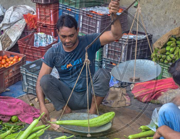 Bareilly, Uttar Pradesh / India - August 27, 2018: Vegetable hawker weighing bottle gourd before sale