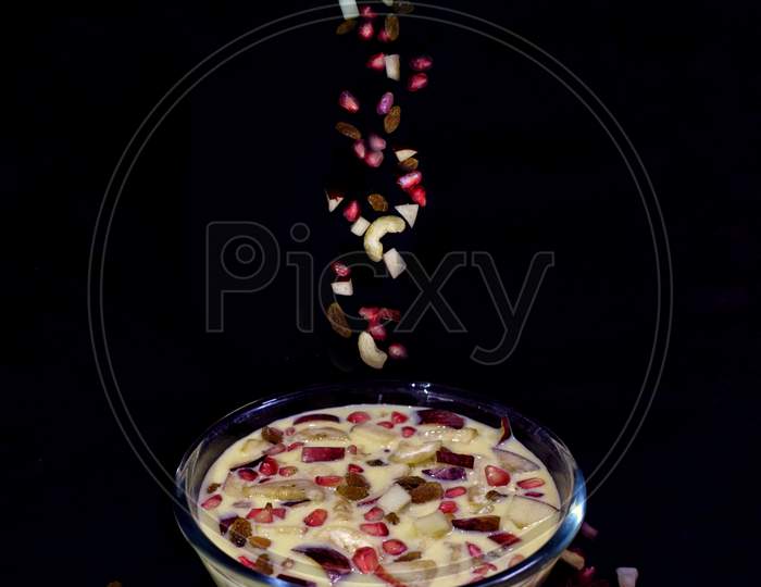 Dry fruits are falling on a bowl of custard on a black background.