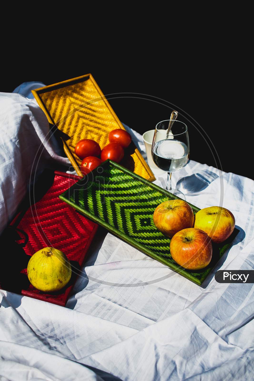 Still Life Of Apples, Pear And Tomatoes Kept On Colorful Exquisite Bamboo Trays Displayed On A White Sheet.