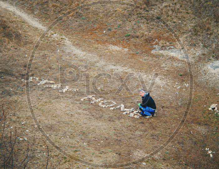 Man creating message "Stay Home" from stones.