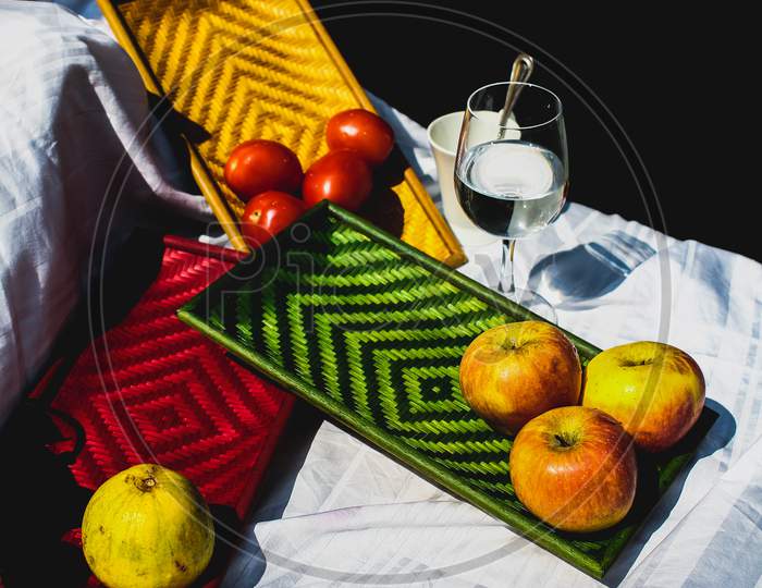Still Life Of Apples, Pear And Tomatoes Kept On Colorful Exquisite Bamboo Trays Displayed On A White Sheet.
