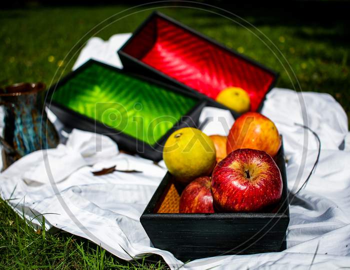 Still Life Of Apples On A Wooden Tray With Two More Colorful Trays In The Background.