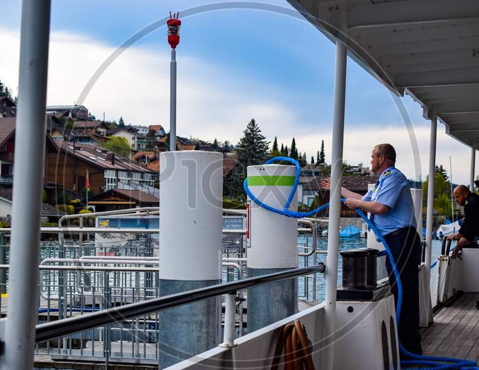 Switzerland, 2019: Man trying tie knot to anchor the boat near harbor.  The boat crew member can be seen throwing the rope in order to hook it in the pillar.