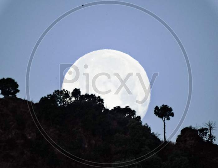 super moon rising behind the hills