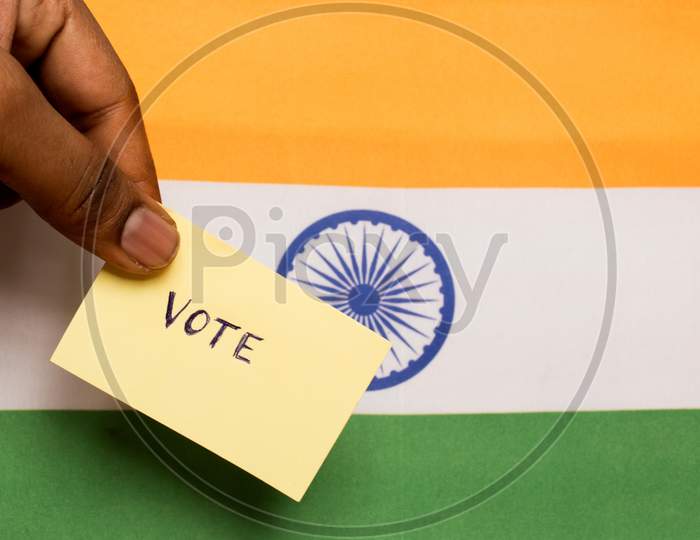 Voting Concept - Person Holding Hand Written Voting Sticker On India Flag.