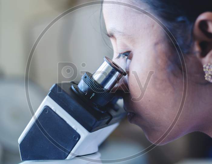 Close Up Of Woman Using A Microscope In A Laboratory - Female Scientist Busy In Looking Into Microscope.