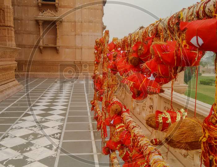 Prayer Coconuts Wrapped In A Red Cloth Tied With Red Threads To The Poles By The Devotees In A Corridor Of A Hindu Temple. Hindu Religious Custom.