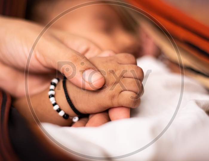 A Newborn Baby Holding The Parent Hand While Sleeping At Cradle