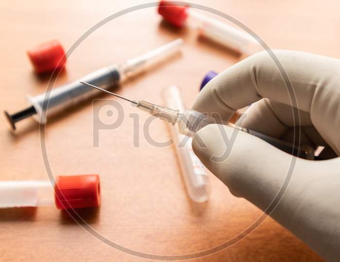 Doctor Hand In White Glove Holding Syringe, To Get Blood Sample In Laboratory With Plain Clot Activators As A Background In India.
