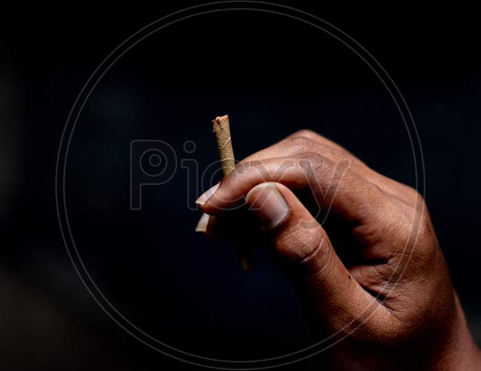 Closeup Of Hands Holding Beedi Or Bidi Cigarette In Dark Room.