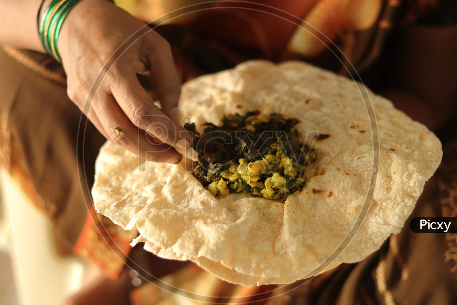 Closeup Of Woman Eating South Indian North Karnataka Peoples Daily Healhy Breakfast Jowar Roti Or Rotti Or Bhakri With Dal Curry In Hand Without Using Plate.