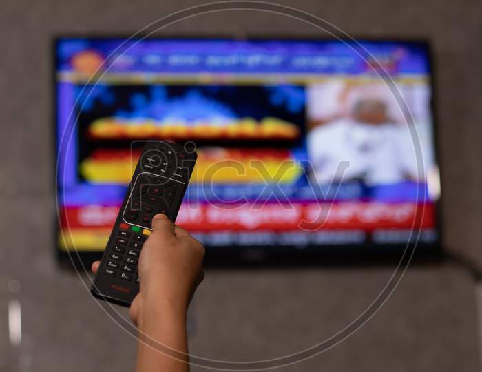 Hands Holding Remote Control Watching News On Tv Screen In Out Of Focus