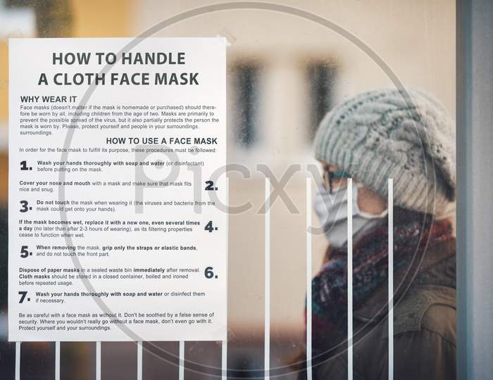 Paper with instructions on how to handle a cloth mask glued at a public transport stop with a woman in the background.