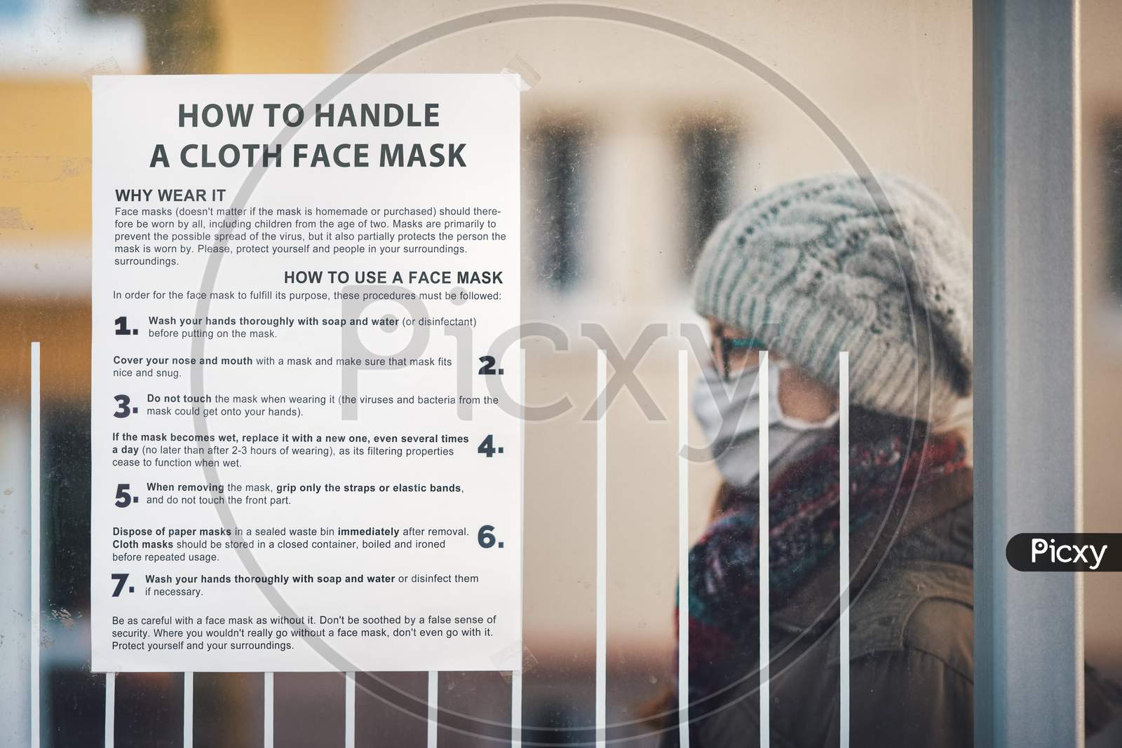 Paper with instructions on how to handle a cloth mask glued at a public transport stop with a woman in the background.