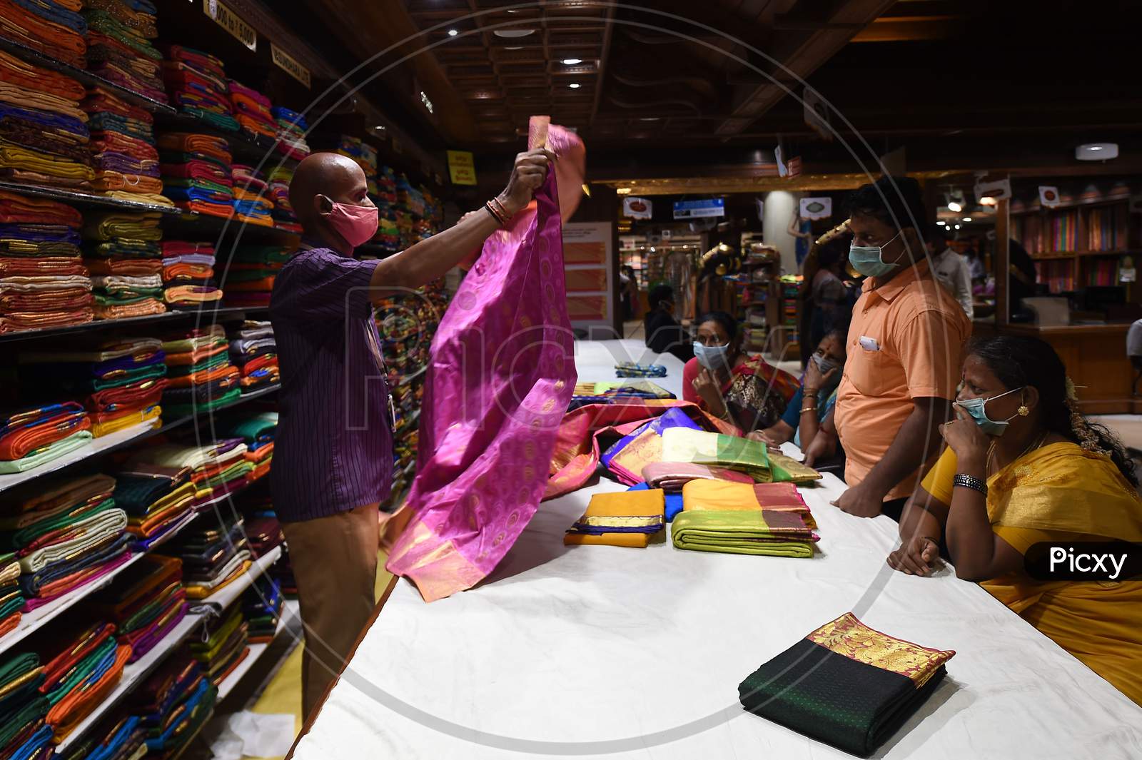 A Salesman Wearing A Face mask Shows A Saree To Customers At A Textile Garment Shop in Chennai, Tamil Nadu