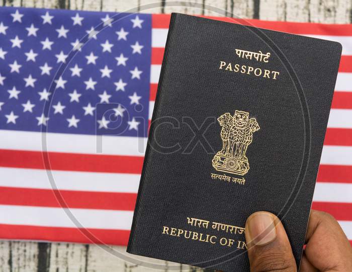 Person Holding Indian Passport With Hand On A Us Or American Flag As Background.