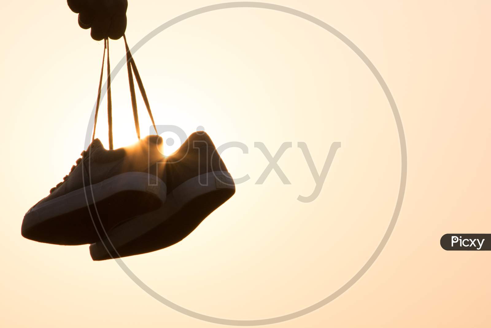 Silhouette Of A Person Holding shoes in Hands With Sun In Background