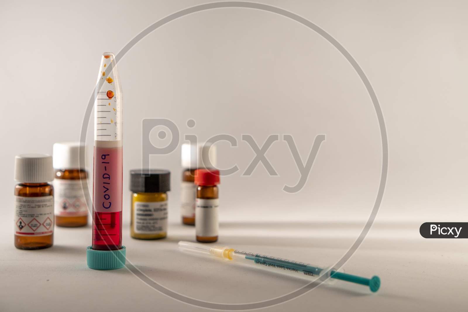Photo concept shows Covid-19 sample in a falcon, and chemicals, and syringe in a blurred background.