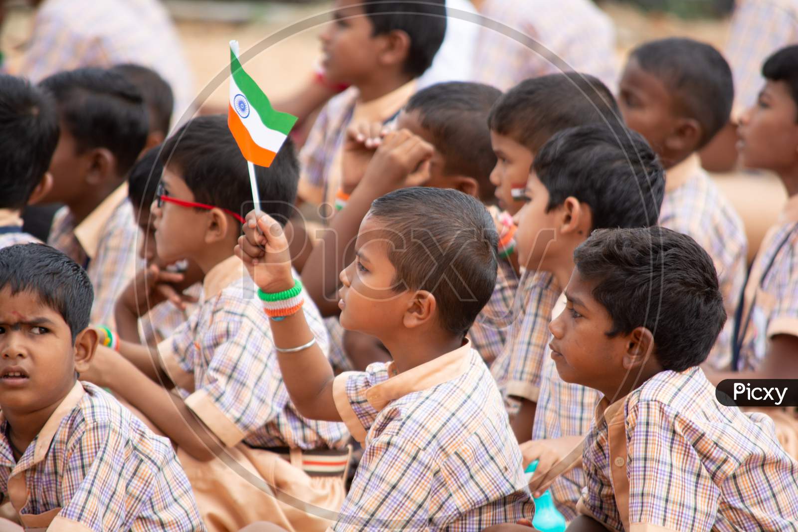 A Group Of Elementary School Kids Sat On Ground By Holding Indian Flag In Hand During Independence Day Of India