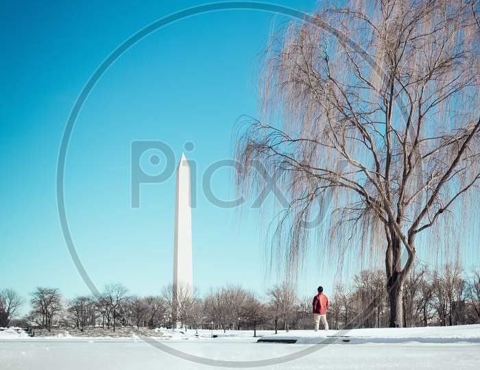 A Man In Red Jacket Watches Washington Monument Standing In Snow During The Day, Washington Dc