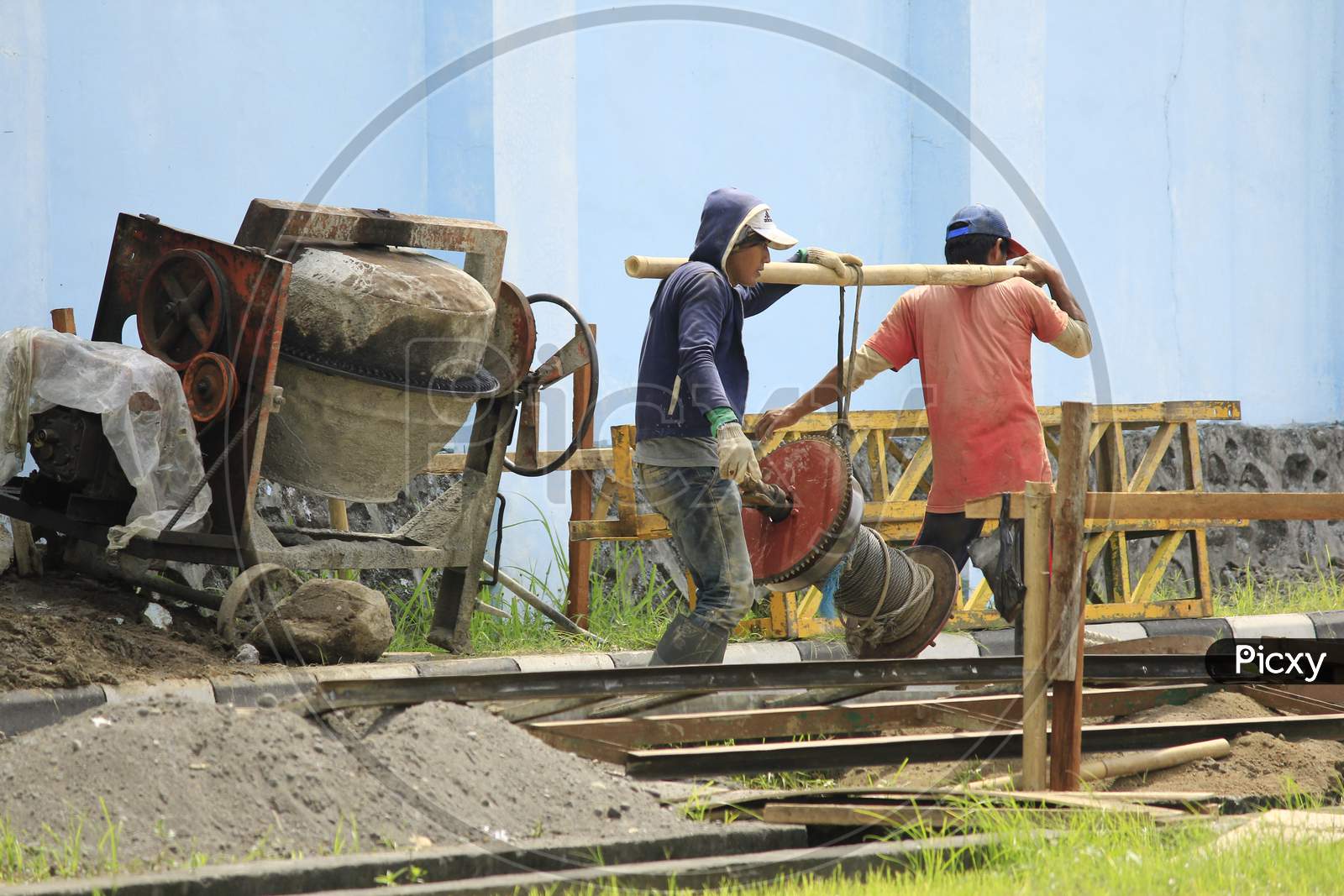 Two construction workers work together to lift steel wire reels