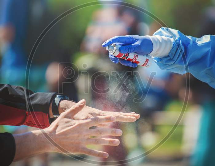 Close-up of a medic hand spraying disinfectant on a man's hands on the street.