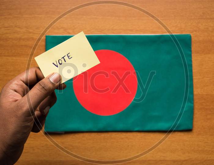 Voting Concept - Person Holding Hand Written Voting Sticker On Bangladesh Flag.