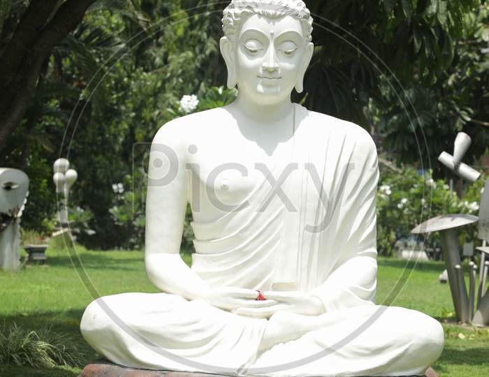 White Buddha Statue In Meditating Posture On Stone Table With Nature As A Background