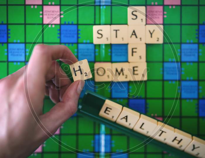 Hand combining the words stay, safe, home and healthy on a scrabble game board. Iconic words calling for social distancing in times of corona crisis.